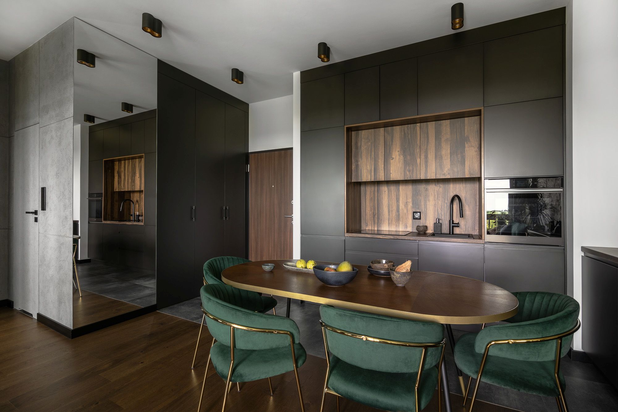 Salon z kuchnią w ciemnej aranżacji z ciemną podłogą i ciemnymi drzwiami wejściowymi.